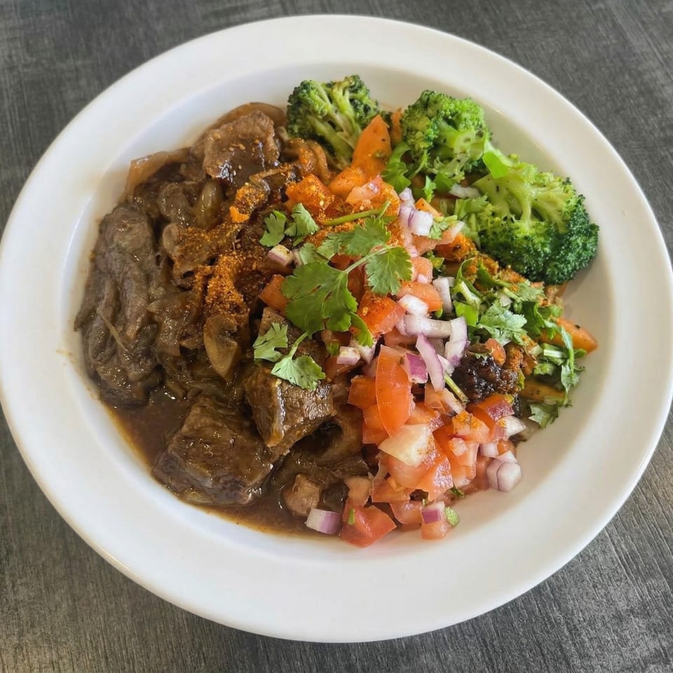 A white bowl filled with beef stew, broccoli, and a fresh tomato and onion salsa.