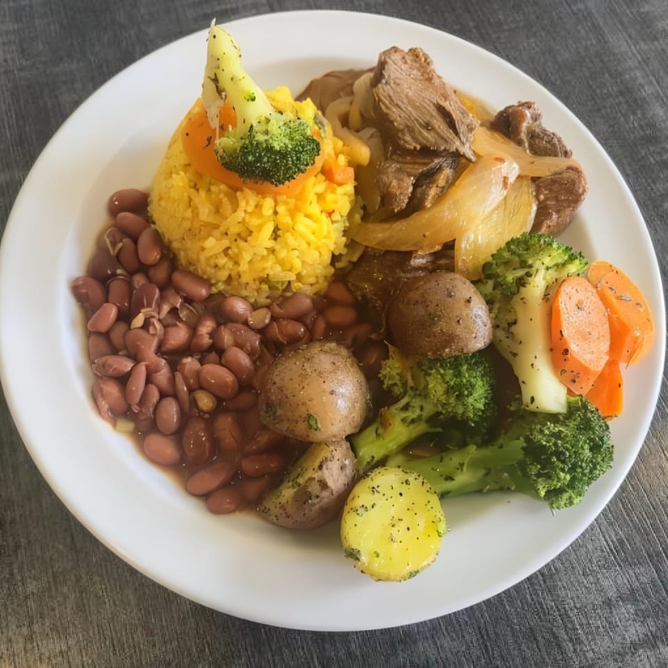 A white plate holds a meal with yellow rice, red beans, beef, potatoes, broccoli, and carrots.
